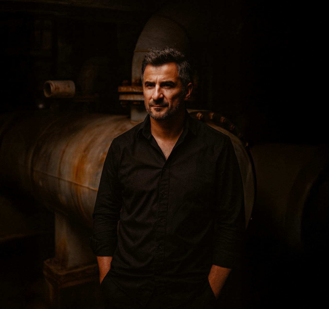 Męski portret biznesowy w czarnej koszuli na tle industrialnego wnętrza, klimatyczne światło i profesjonalna fotografia wizerunkowa.